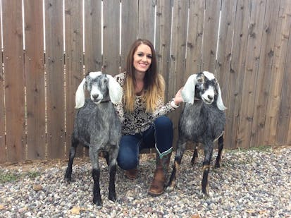 Woman posing with two grey and white goats